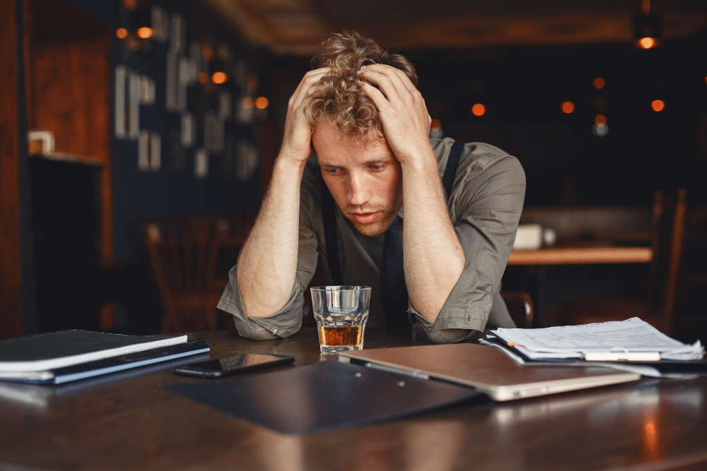 Man drinking whiskey at a cluttered desk, illustrating alcohol use before the alcohol withdrawal timeline begins.